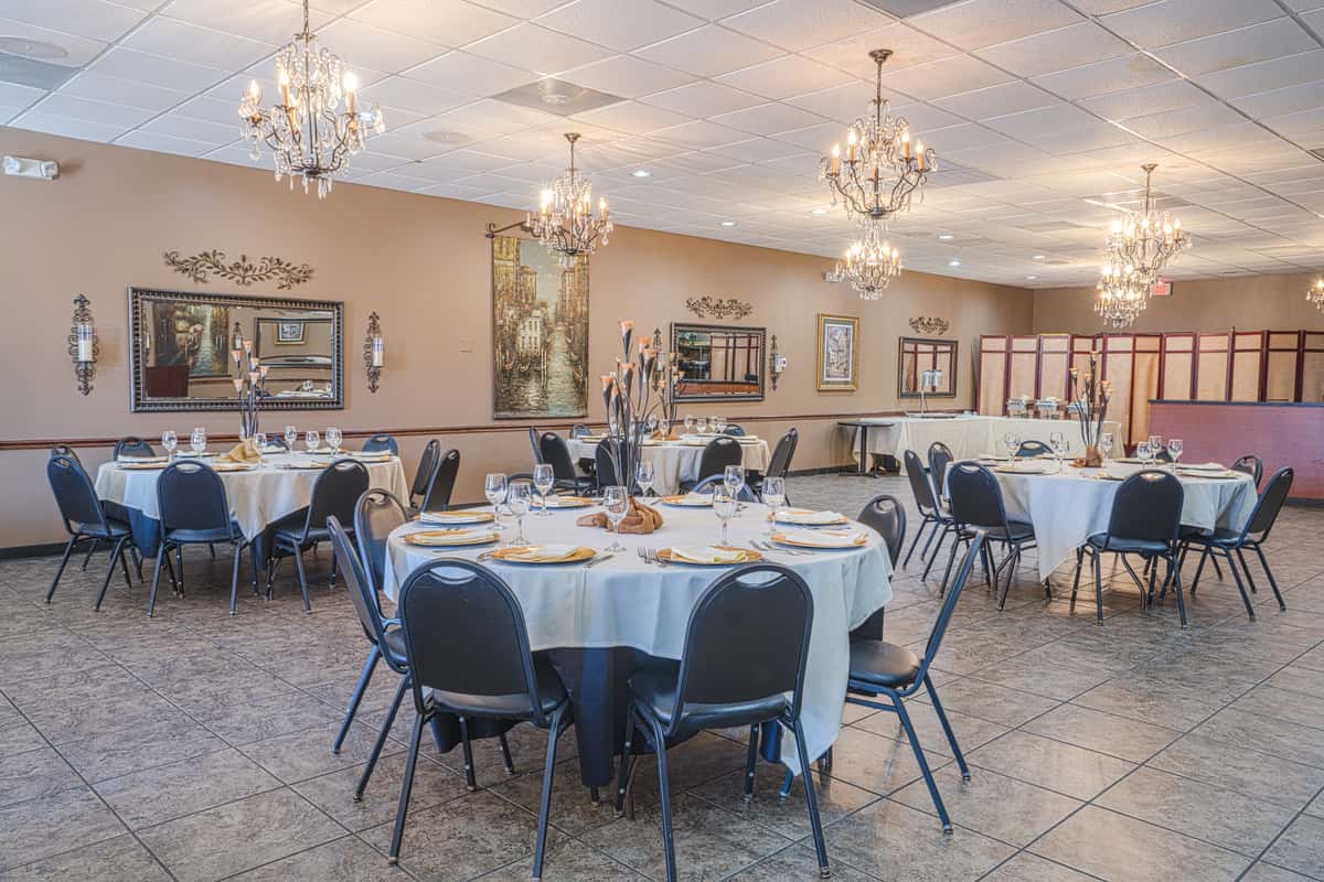 Elegant banquet hall with round tables, white linens, blue chairs, chandeliers, and framed artwork on beige walls