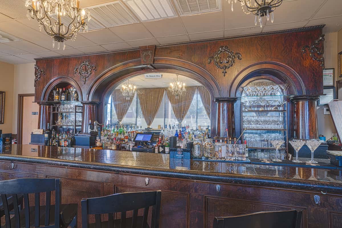 Elegant wooden bar with arched mirrors, chandeliers, liquor bottles, and glassware in upscale restaurant interior