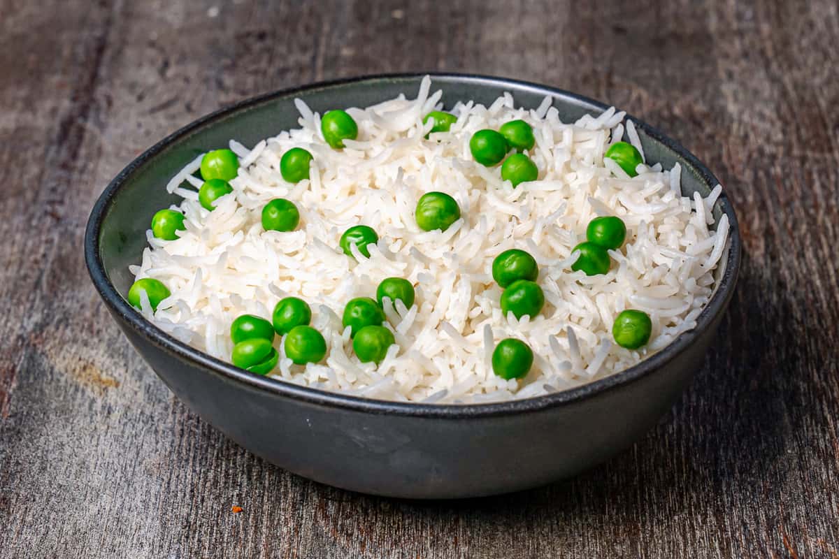 Steamed basmati rice with green peas served in a rustic bowl on a wooden table.