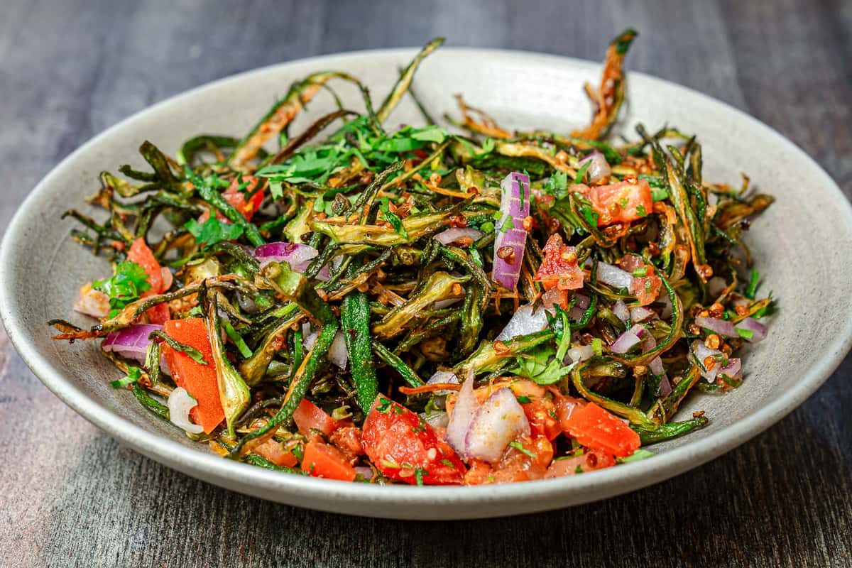 Crispy fried okra (bhindi) salad tossed with chopped tomatoes, red onions, fresh herbs, and spices, served as a vibrant Indian-style vegetable appetizer in a rustic bowl.
