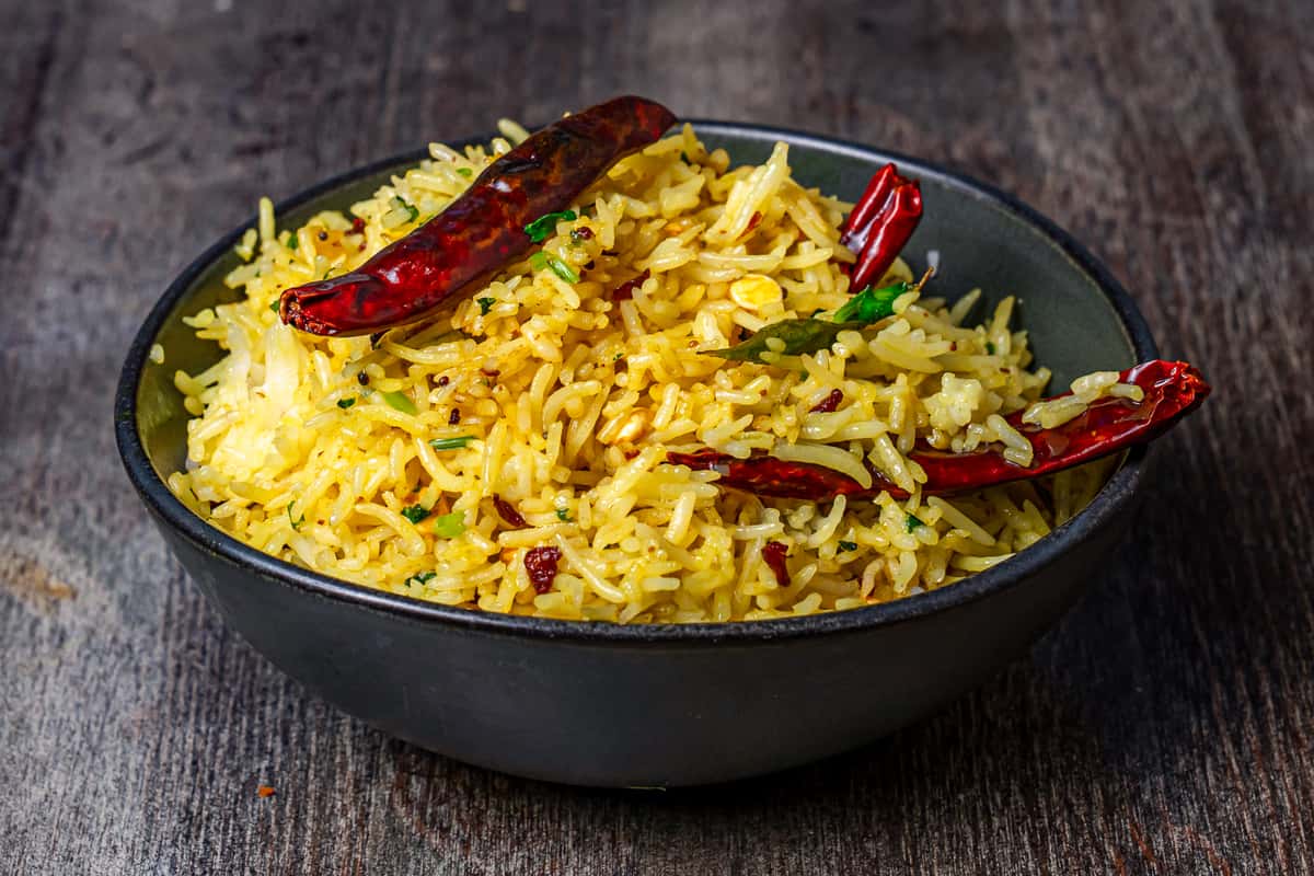 Spiced Indian lemon rice in a black bowl, featuring fluffy basmati rice tossed with mustard seeds, curry leaves, peanuts, and whole dried red chilies—classic South Indian rice dish presentation.