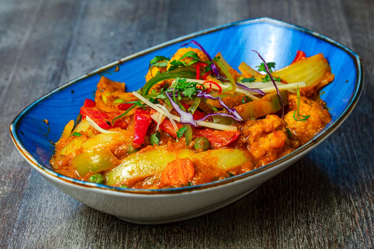 Mixed vegetable curry with bell peppers, peas, and herbs served in a blue bowl.