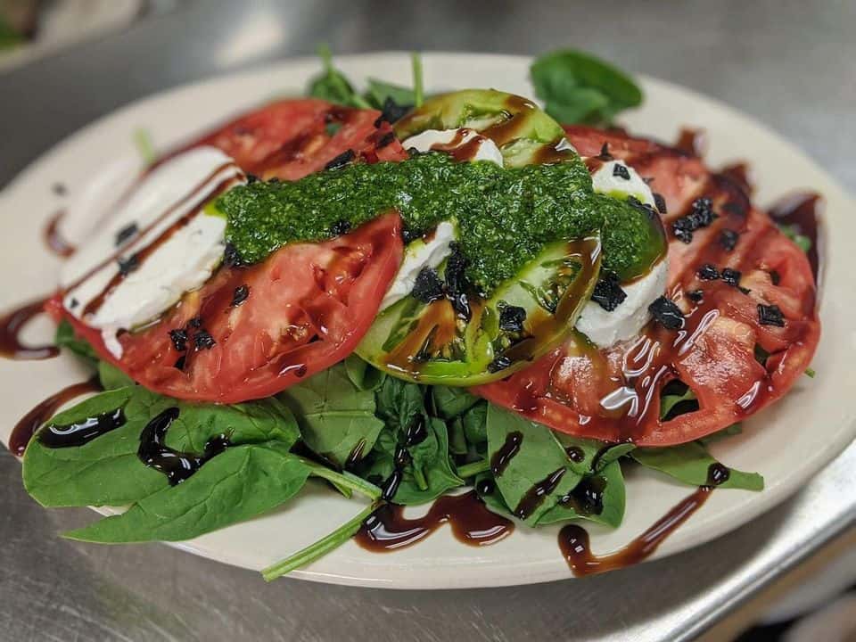 Caprese Salad featuring heirloom tomatoes, fresh mozzarella, nut free pesto, balsamic reduction, baby spinach and black salt.