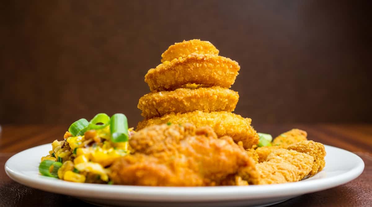 Golden-brown fried chicken nuggets and onion rings stacked on a white plate, with chopped green onions.