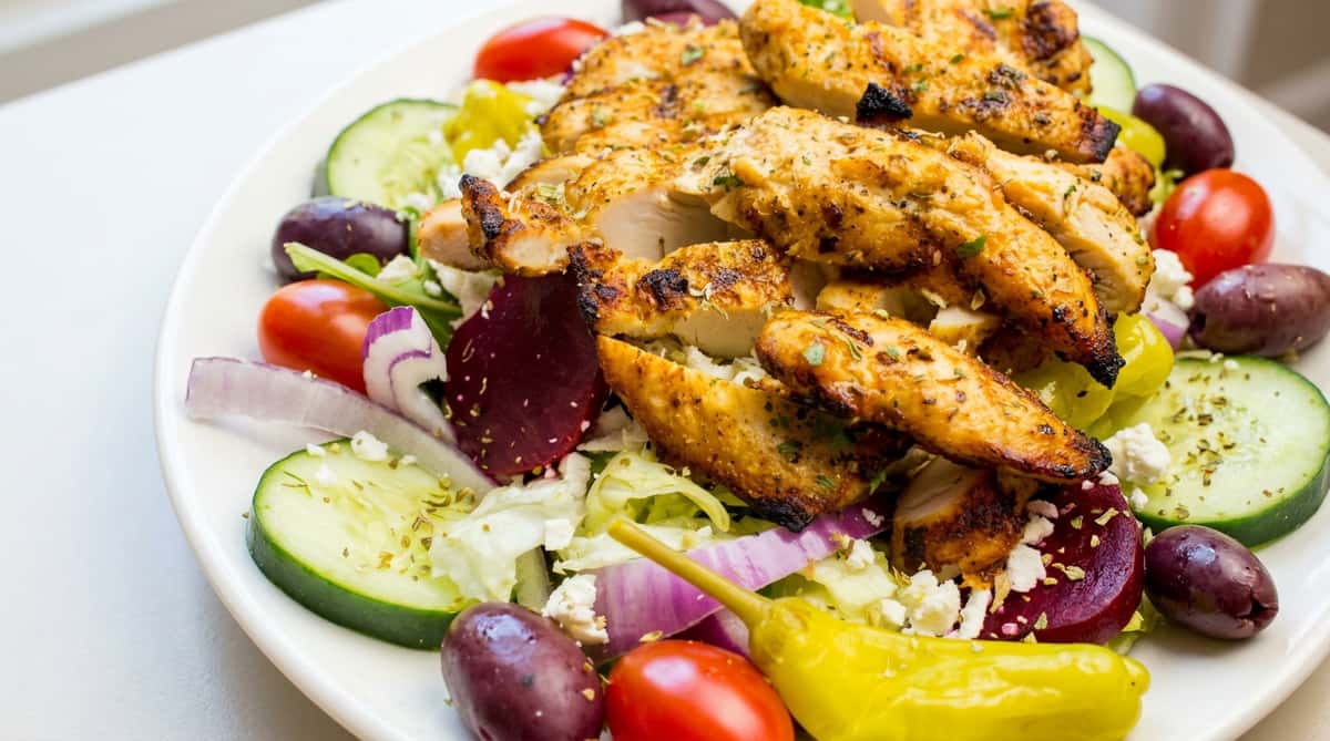 Greek salad with grilled chicken, tomatoes, cucumbers, red onion, olives, feta, and a pepperoncini.