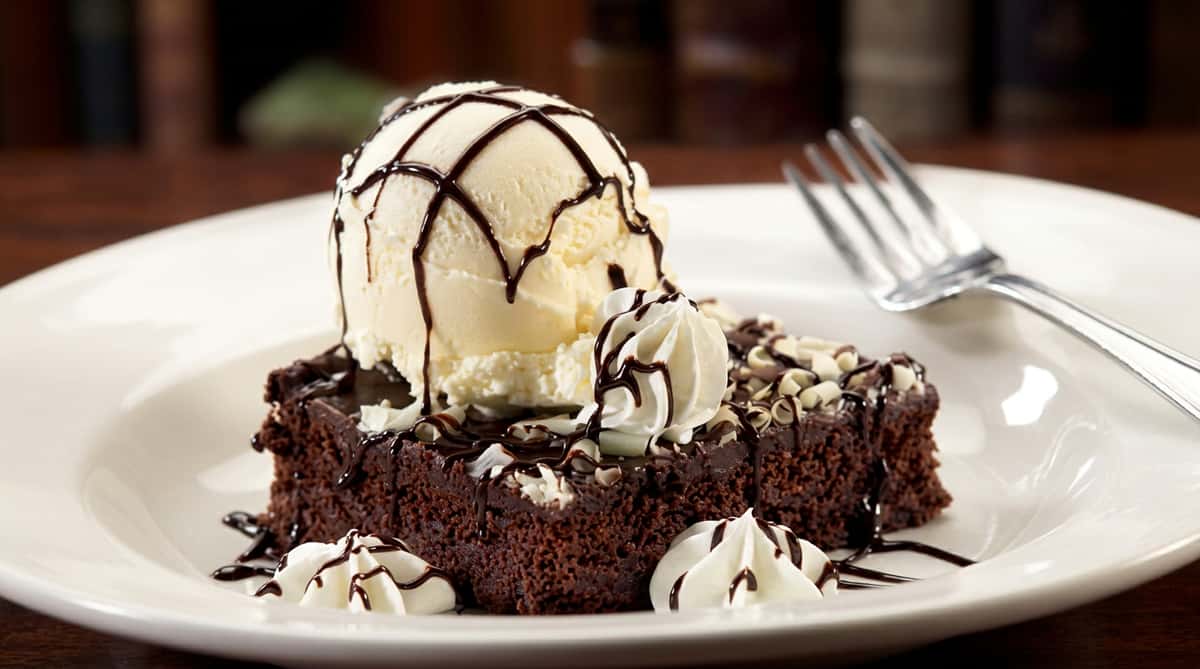 Chocolate brownie topped with a scoop of vanilla ice cream, chocolate drizzle, and whipped cream swirls.