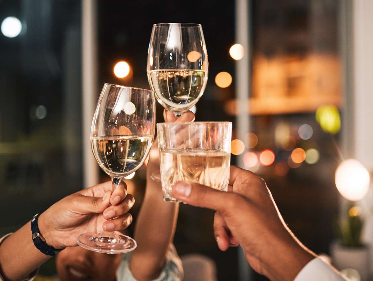 Guests raising glasses of wine and cocktails in a celebratory toast, capturing an upscale dining experience and vibrant restaurant atmosphere.