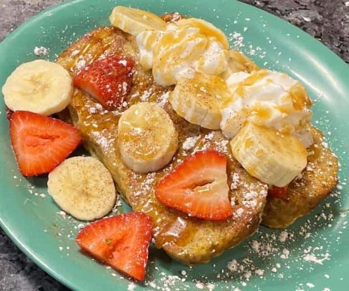 french toast with strawberries, bananas, whipped cream and maple syrup.