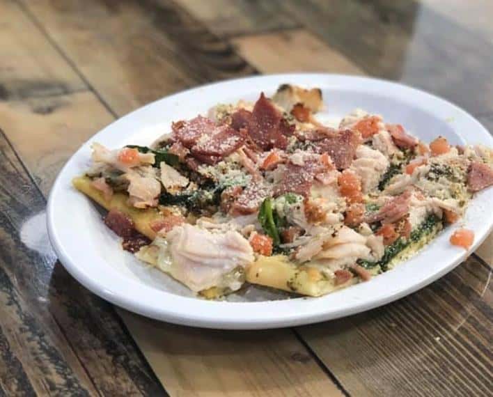 flatbread with meats, cheese, spinach and chopped tomato.