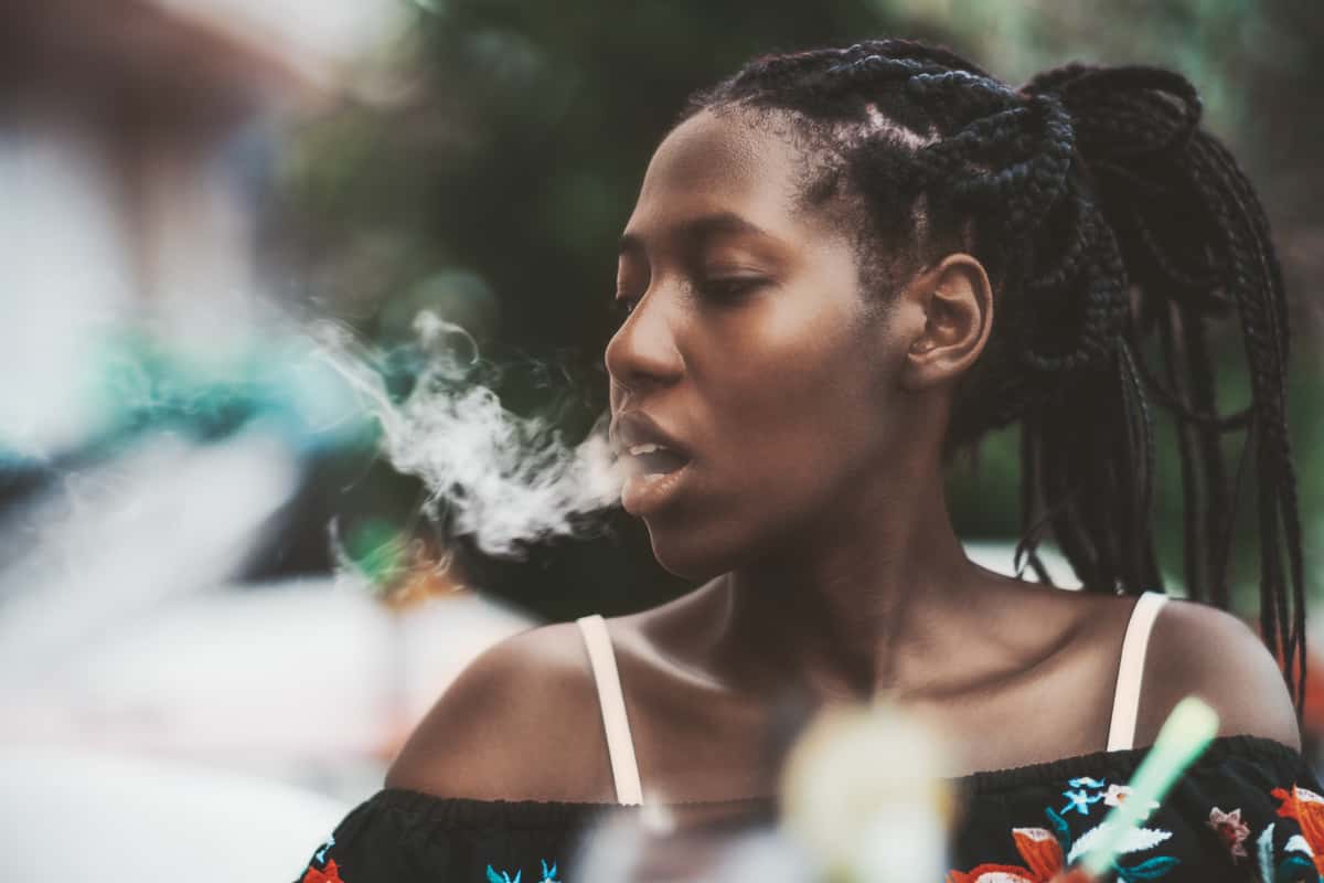 Candid outdoor shot of a young woman with braided hair exhaling hookah smoke