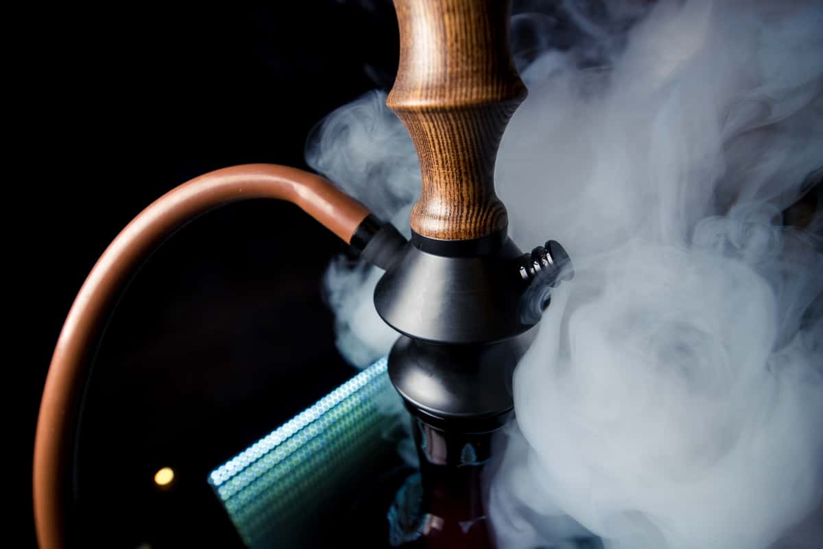 Detailed close-up of a modern, stylish hookah with rich wooden and black metal accents, enveloped in thick, white smoke