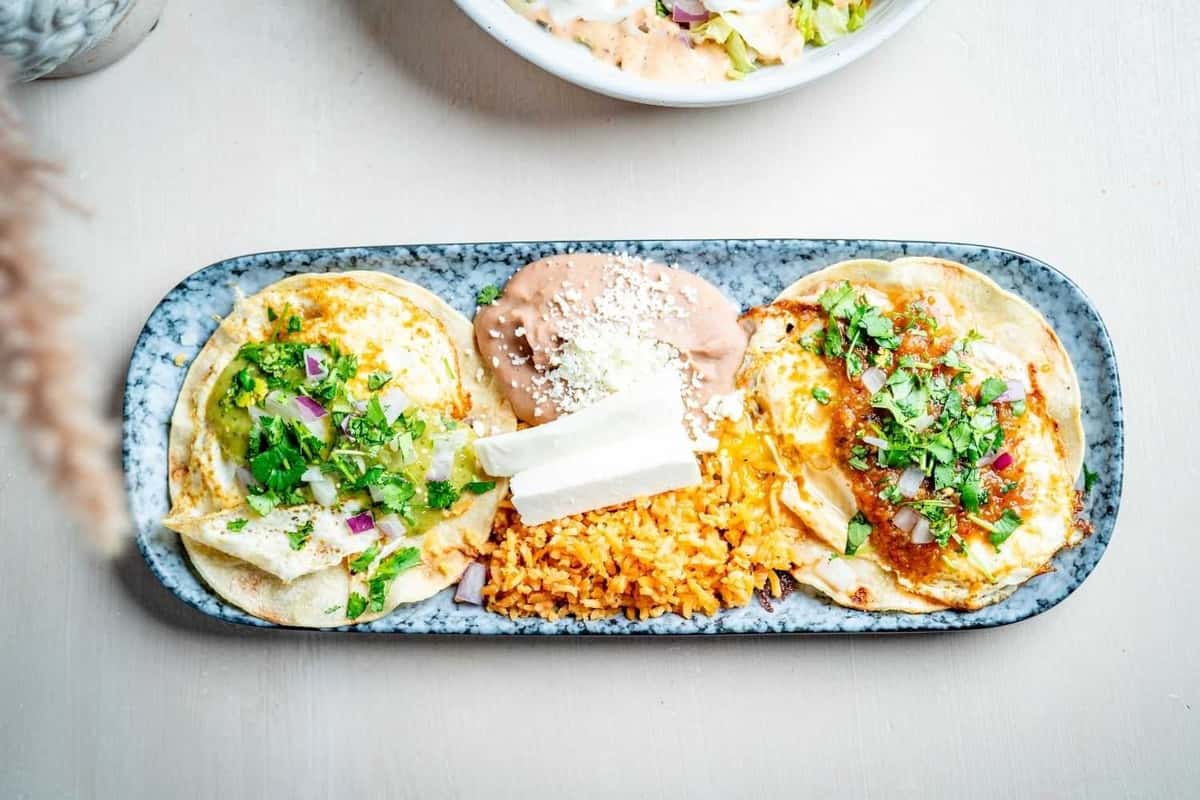 Authentic Mexican taco platter with soft corn tortillas filled with eggs, salsa, fresh cilantro, and onions, served with rice and refried beans for a colorful brunch-style presentation.