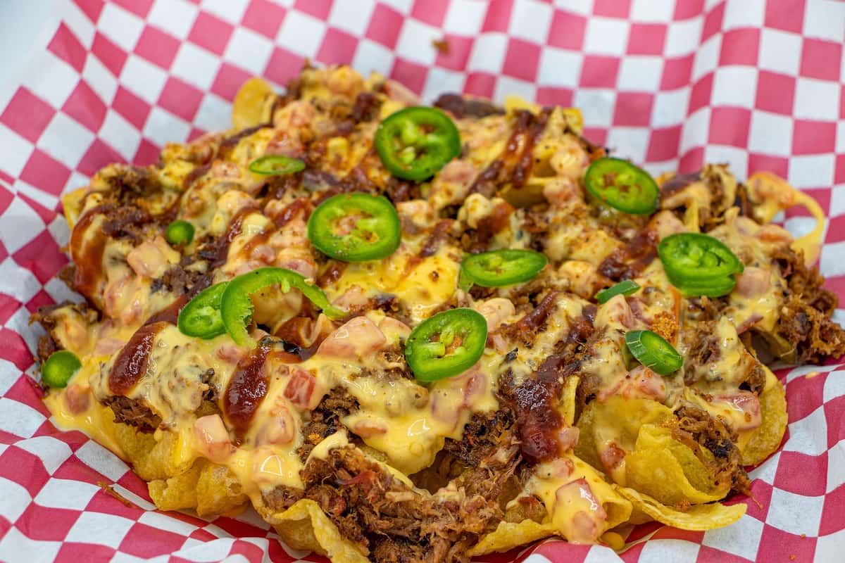 Loaded BBQ nachos piled high with melted cheese, pulled meat, jalapeño slices, and tangy sauce on crispy tortilla chips, served in a casual comfort food setting.