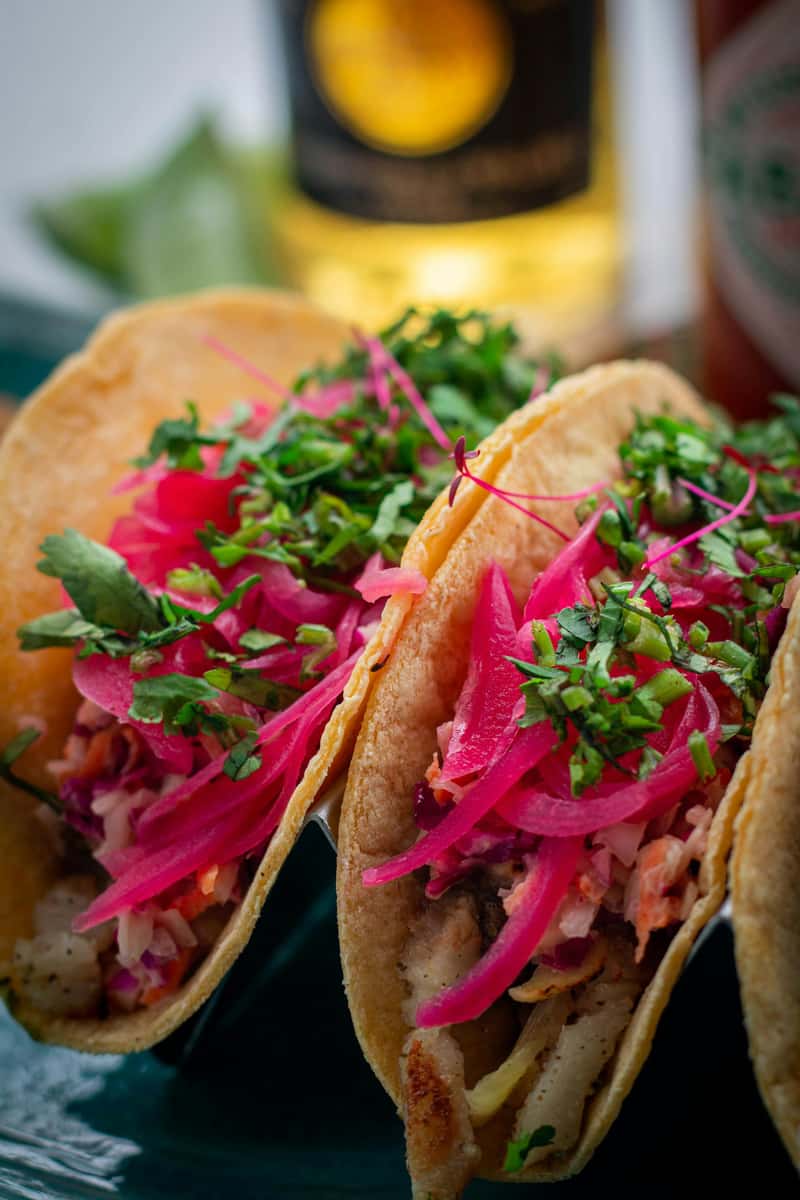Fresh fish tacos topped with vibrant pickled red onions, cilantro, and slaw on soft corn tortillas, showcasing bright coastal Mexican flavors.