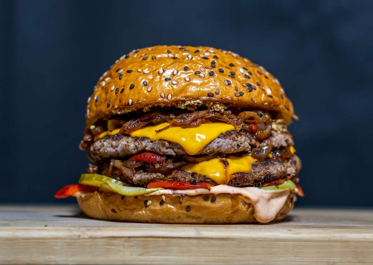 Loaded double cheeseburger with layered beef patties, melted cheddar, pickles, and house sauce on a sesame seed bun, styled for a bold, indulgent comfort food experience.