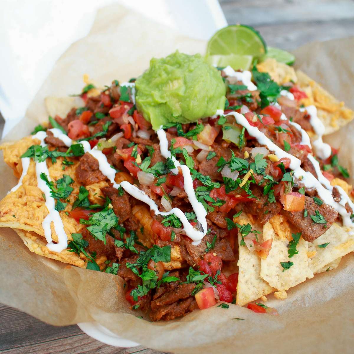 Hearty nachos topped with grilled steak, fresh pico de gallo, guacamole, and drizzled crema on crispy tortilla chips, perfect for sharing.