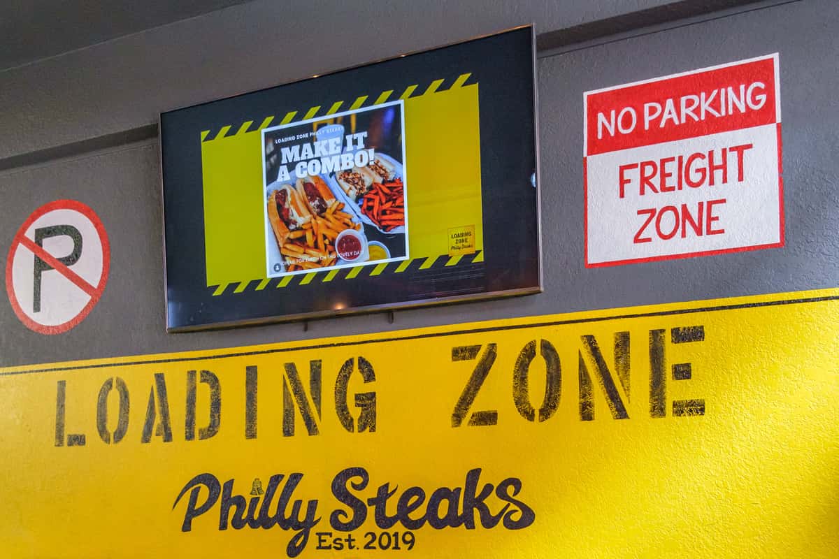 Yellow wall sign saying 'Loading Zone Philly Steaks'