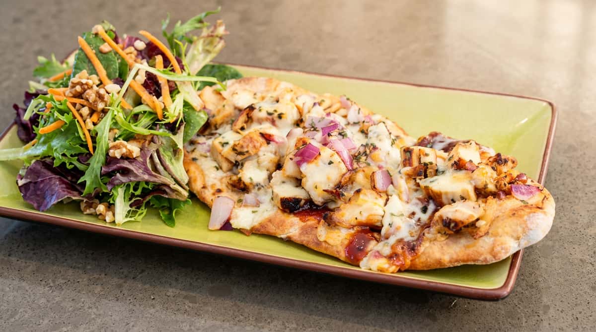 Chicken flatbread with melted cheese, red onion, and herbs, served with a side salad.