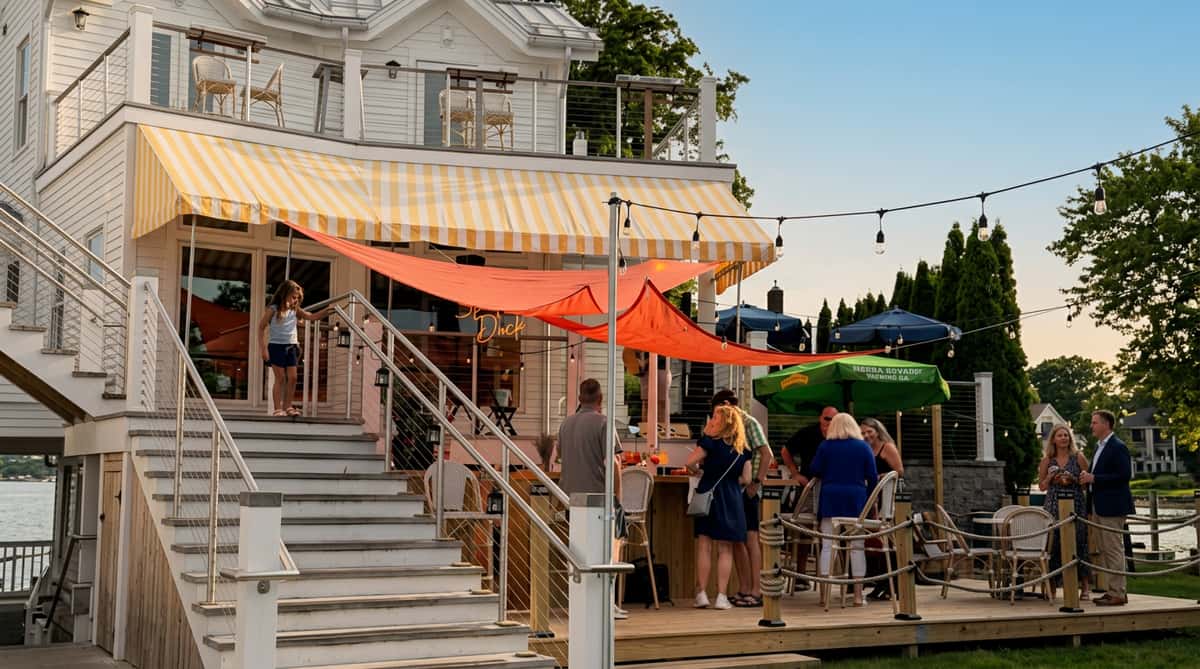 Outdoor bar and patio with people on a wooden deck under orange and yellow striped awnings.