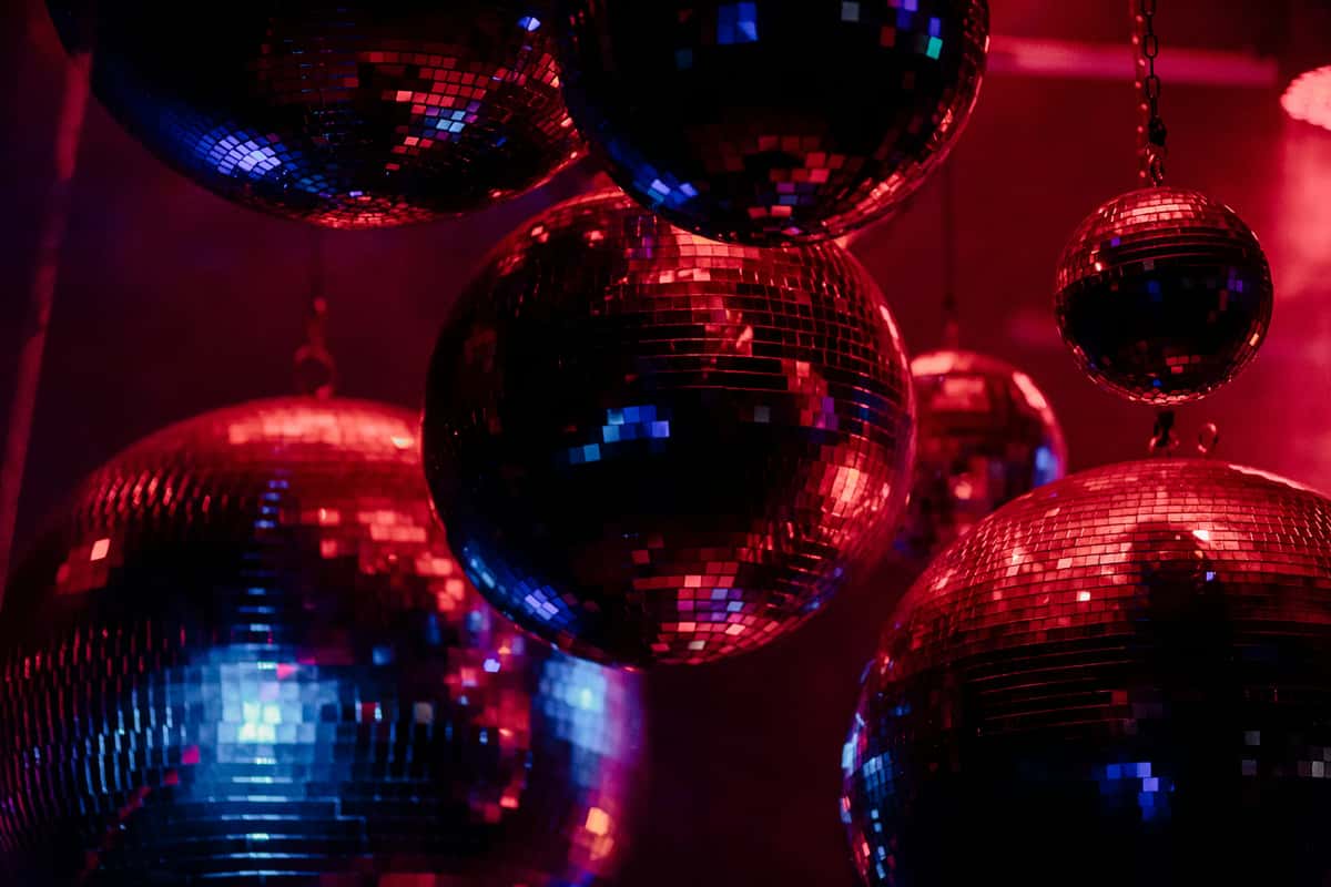 Cluster of mirrored disco balls hanging from the ceiling, reflecting vibrant red and blue nightclub lighting.