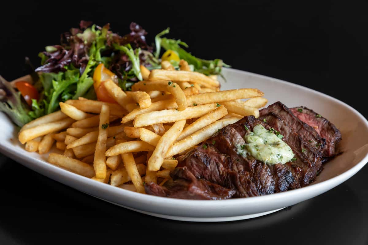 Grilled steak frites served with crispy French fries, mixed greens salad, and herb butter on a white platter.