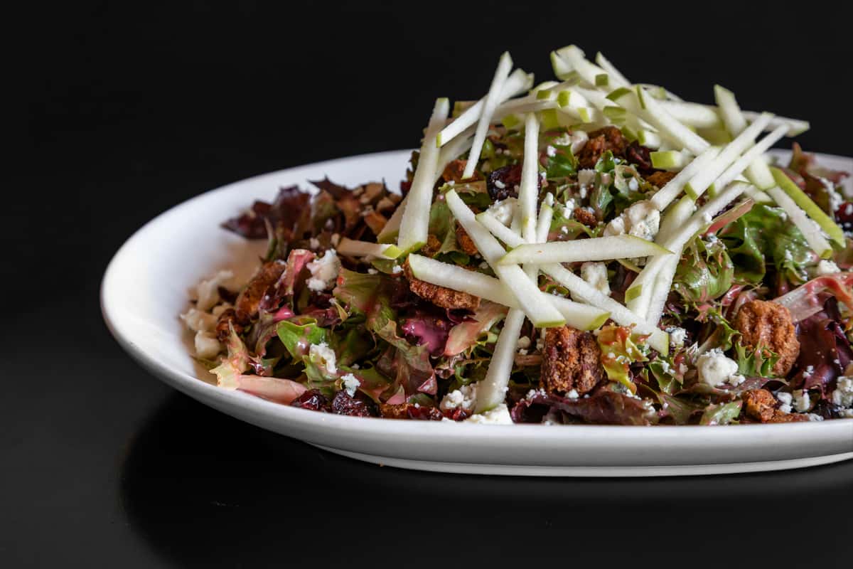 Fresh mixed greens salad topped with crisp apple matchsticks, candied pecans, dried cranberries, crumbled goat cheese, and house vinaigrette.