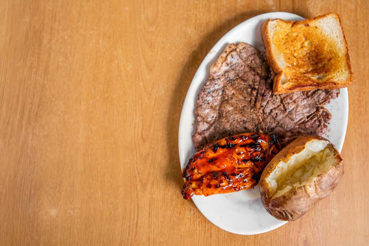 Grilled steak and chicken with toast and a baked potato, viewed from above.
