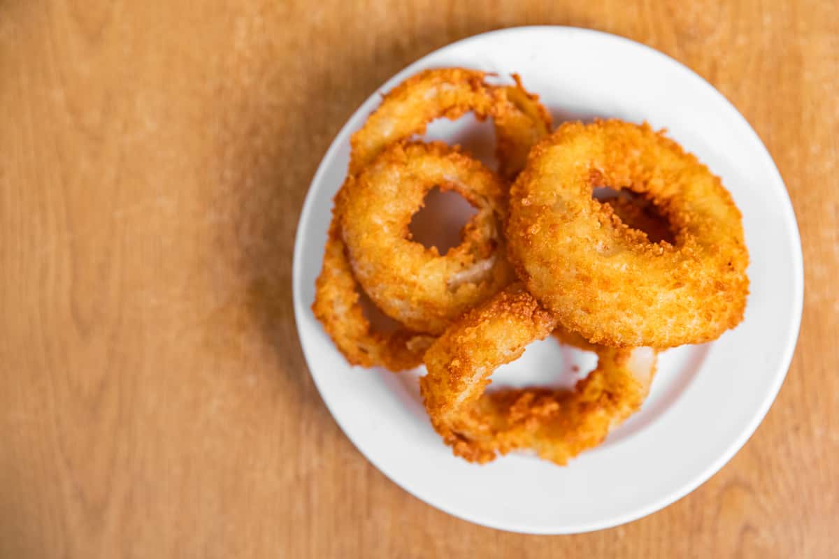Breaded onion rings on a white plate, viewed from above.