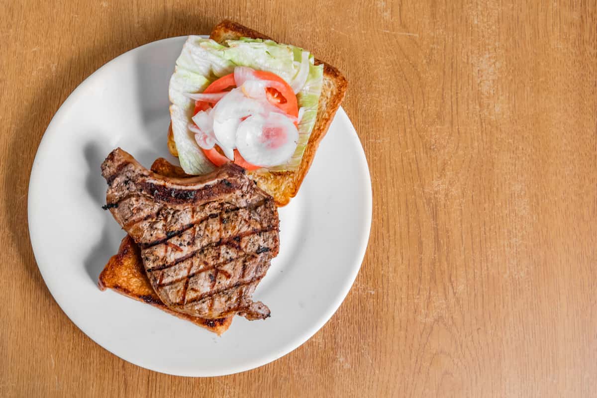 Open-faced steak sandwich with lettuce, tomato and onion on toast.