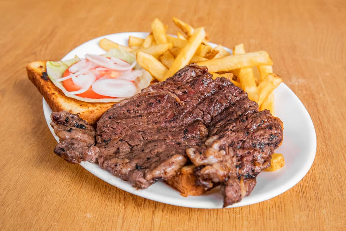Grilled steak sandwich served open-faced with fries, lettuce, tomato and onion.