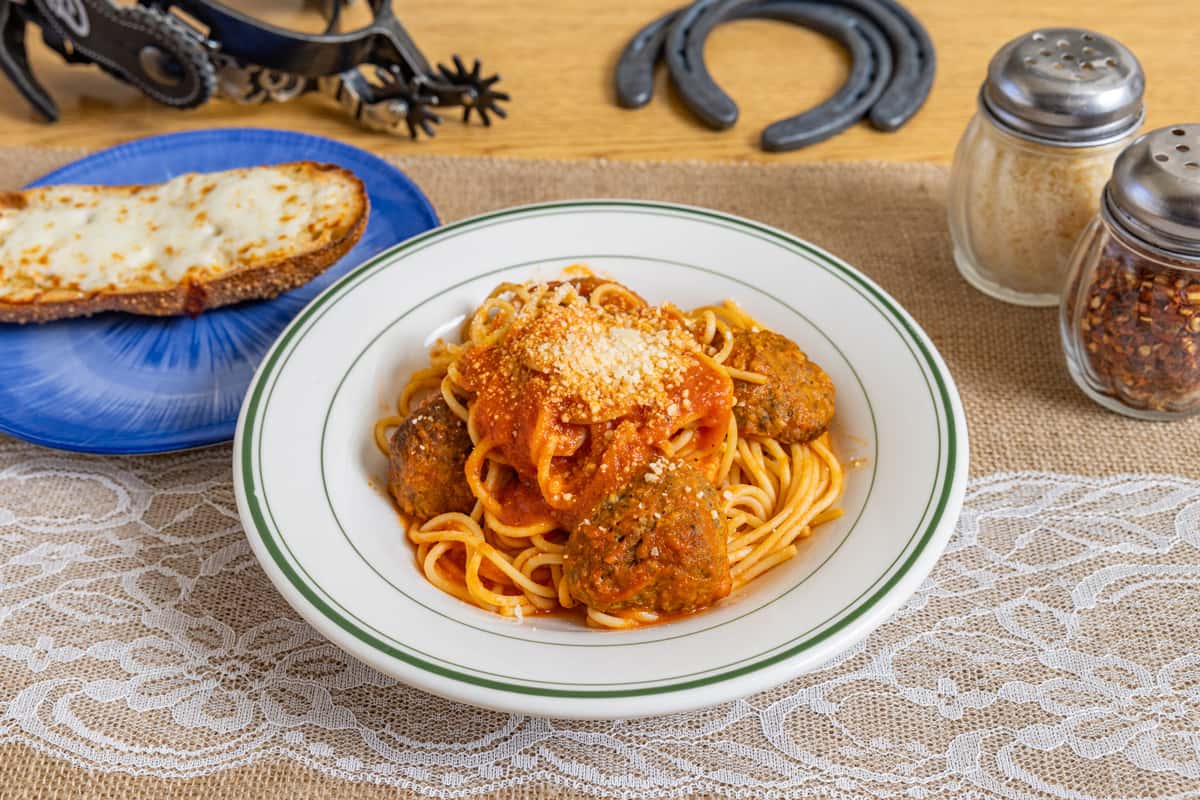 Classic spaghetti and meatballs smothered in marinara sauce and sprinkled with Parmesan cheese, served in a white ceramic bowl with a slice of toasted cheese bread and traditional Italian seasonings.