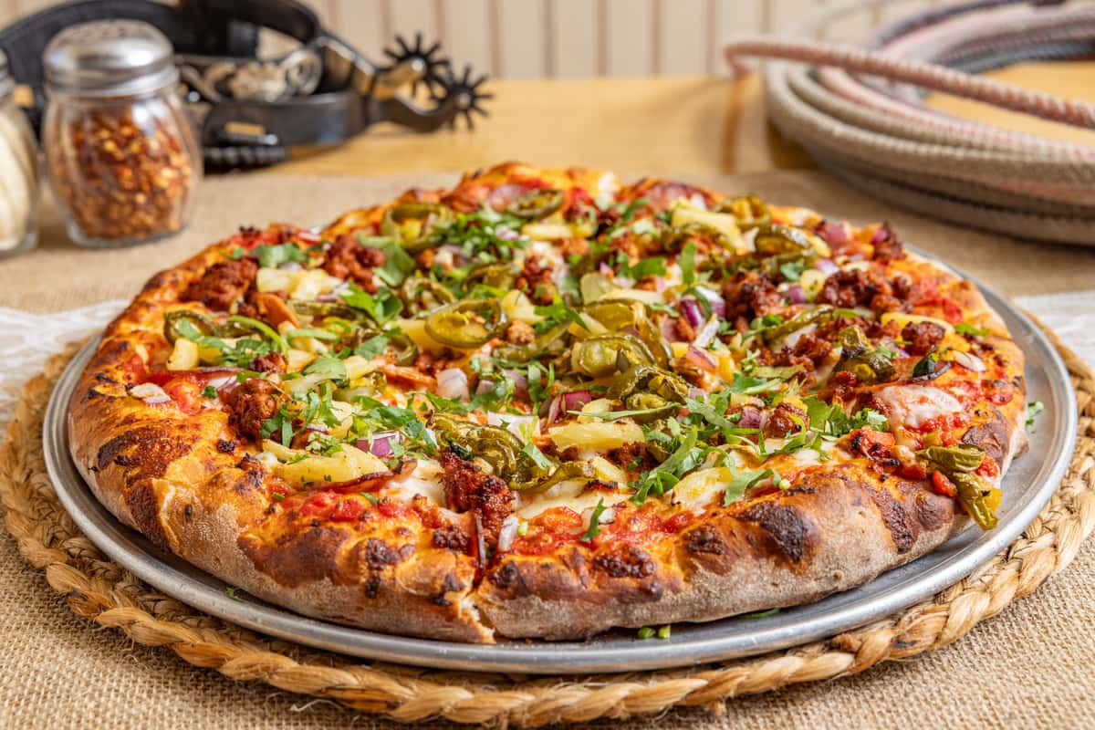 Spicy pizza with sausage, jalapeños, pineapple, red onions, and chopped cilantro on a golden, crispy crust.