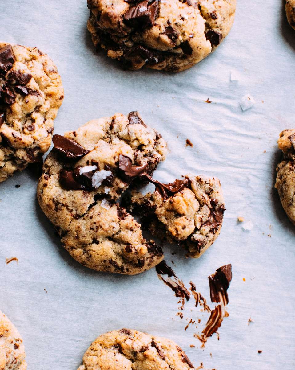 Gooey chocolate chip cookie broken open on parchment paper with melted chocolate and flaky sea salt, featuring decadent bakery-style cookies with a soft center.