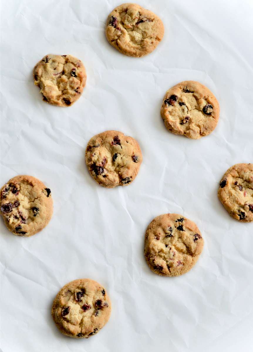 Soft-baked cranberry white chocolate cookies spaced on parchment paper, featuring chewy homemade bakery cookies with tart dried cranberries and sweet chocolate chunks.