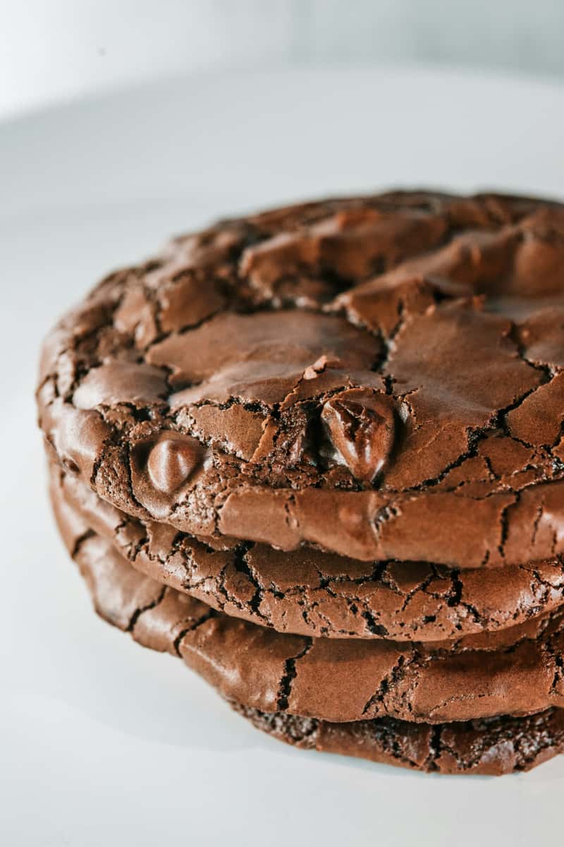 Stacked fudgy brownie cookies with crackled tops and glossy chocolate finish, featuring rich double chocolate bakery cookies with a chewy, decadent texture.
