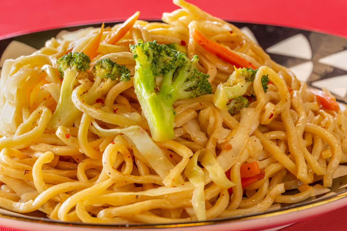 Close-up of a savory stir-fried noodle dish featuring thick lo mein noodles tossed with broccoli, cabbage, and carrots in a light soy-based sauce. Perfect for Asian cuisine menus and takeout promotions.