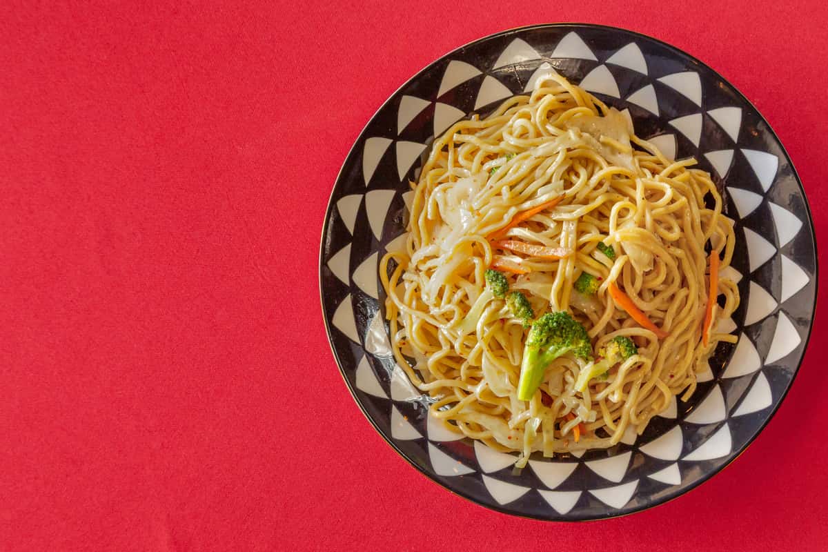 Top-down view of a vibrant vegetable lo mein dish served on a patterned black and white plate, featuring stir-fried noodles with broccoli, cabbage, and carrots—perfect for highlighting classic Chinese takeout or dine-in cuisine.