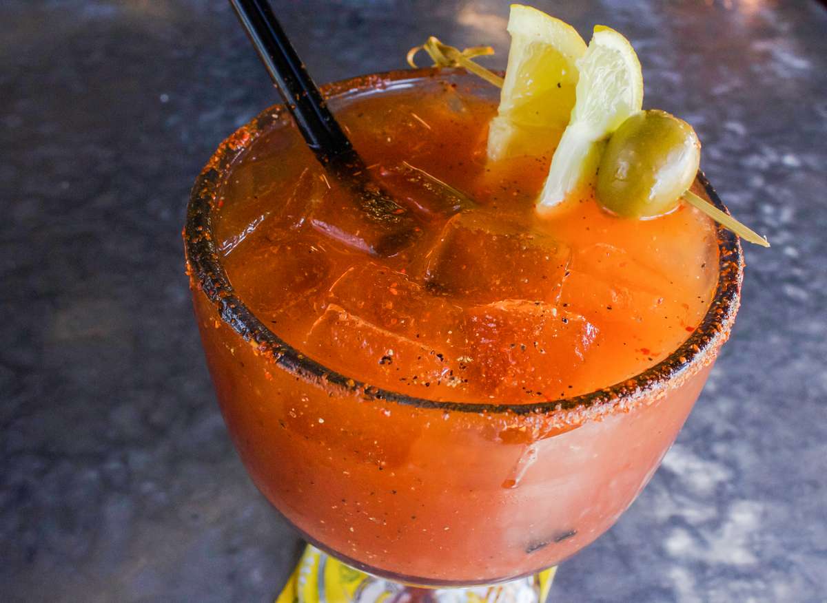 Michelada in a schooner glass with lemon and olive garnish and tajin rim.