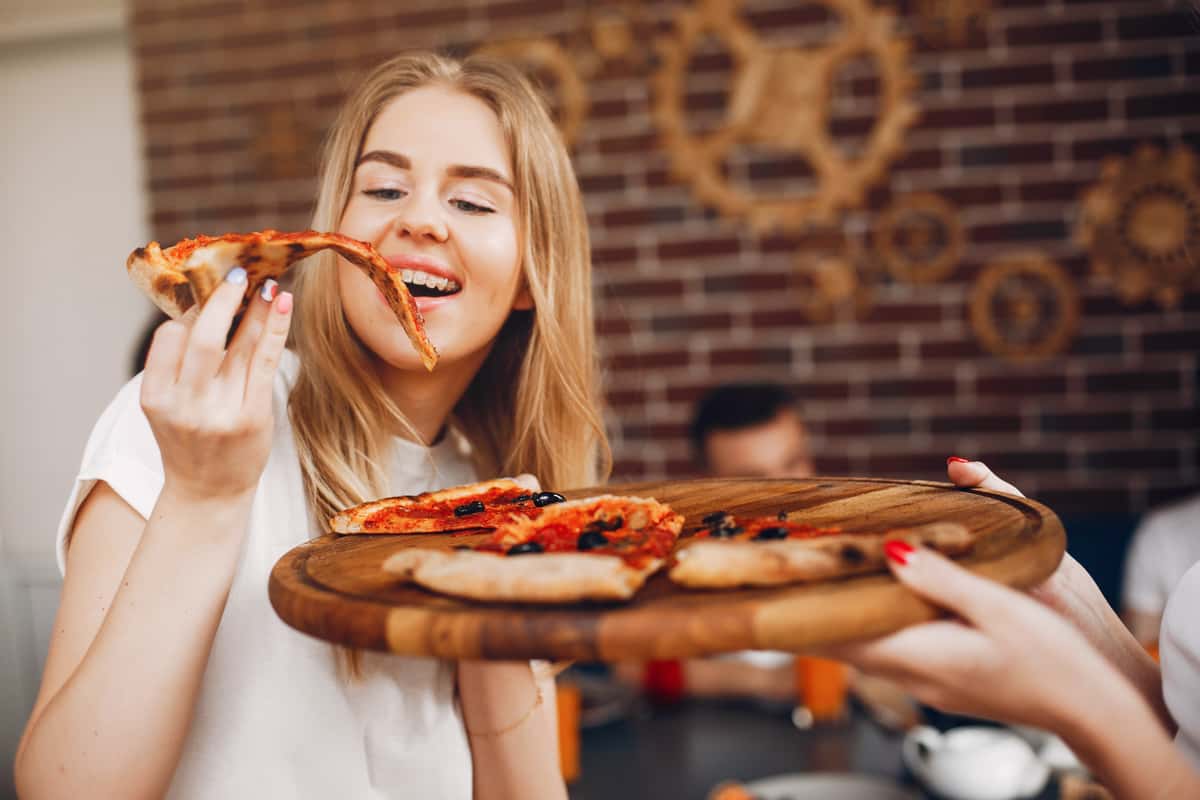 Young woman enjoying a slice of pizza while holding a platter of pizza slices