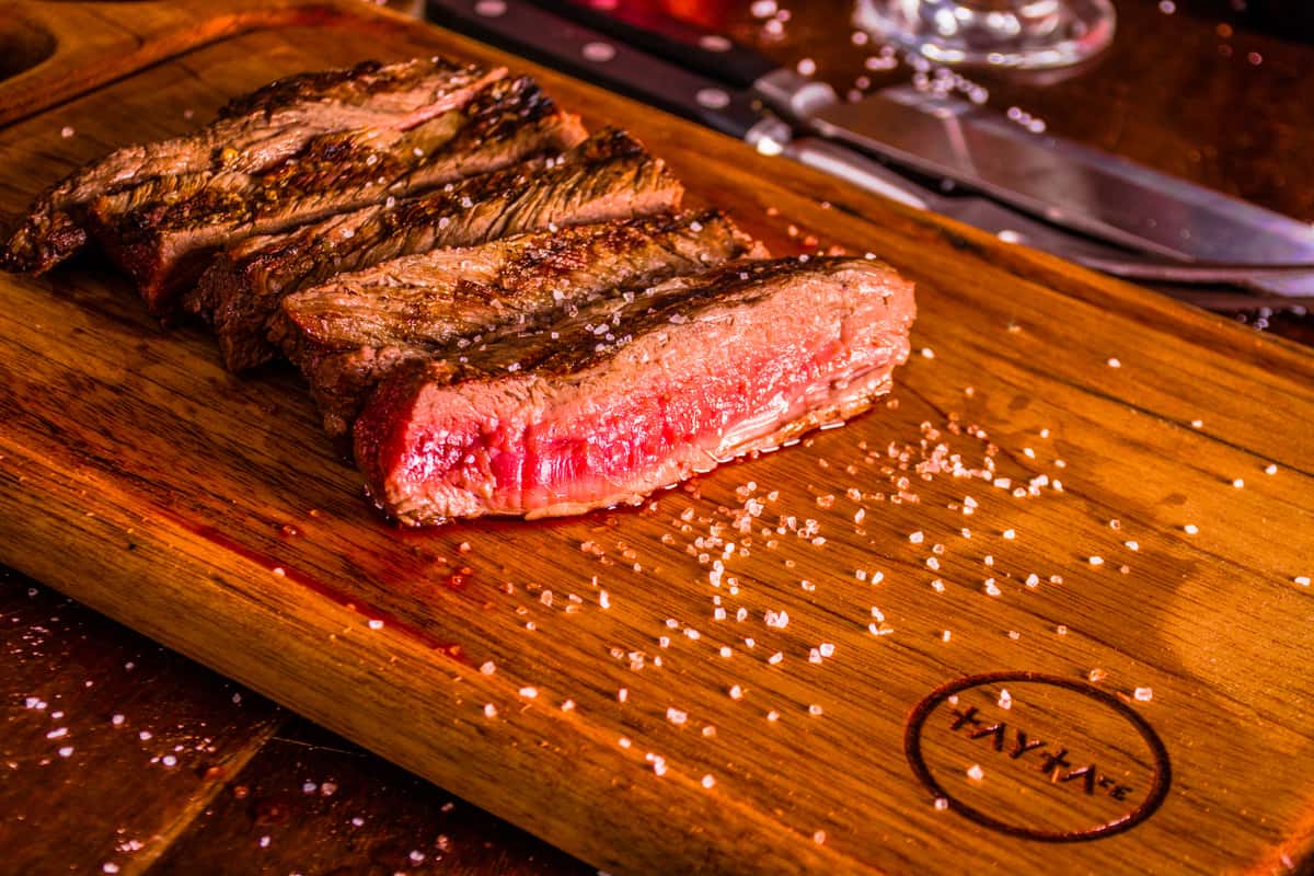 Strips of medium-rare grilled steak arranged on a wooden board, sprinkled with coarse salt.