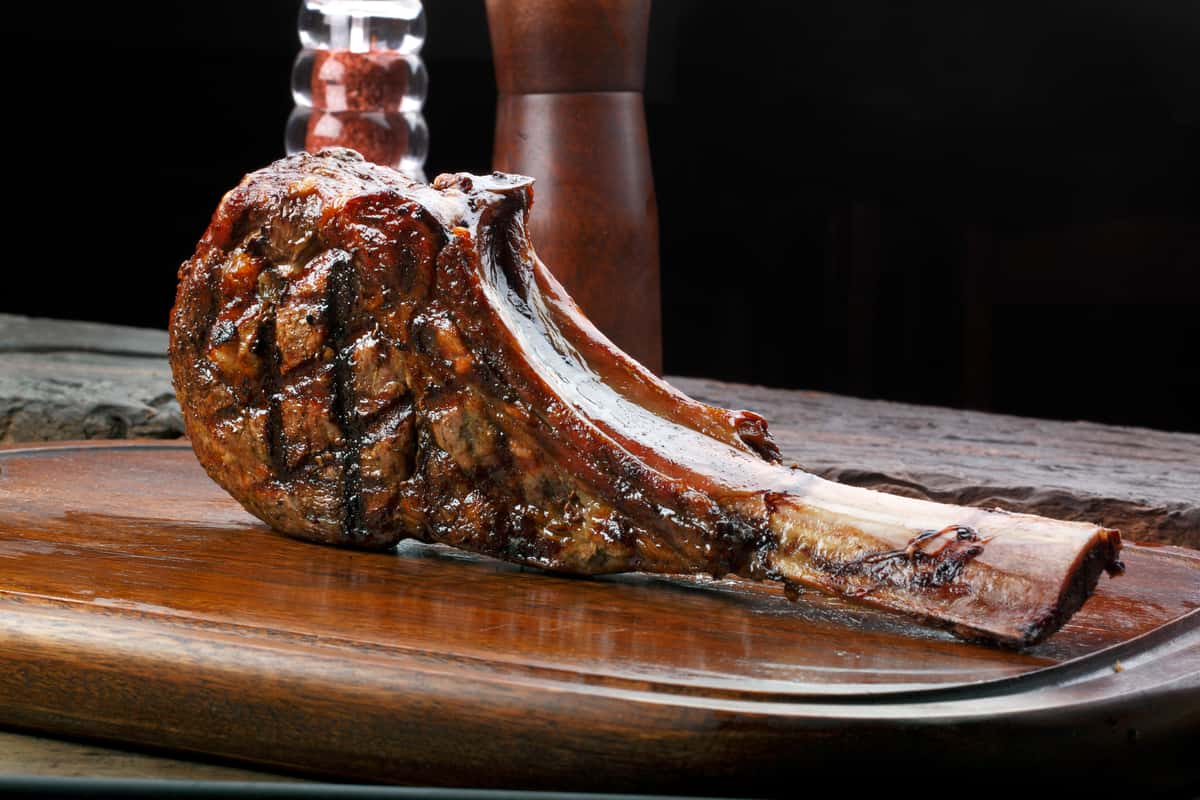 A large, grilled bone-in Tomahawk ribeye steak resting on a wooden cutting board.