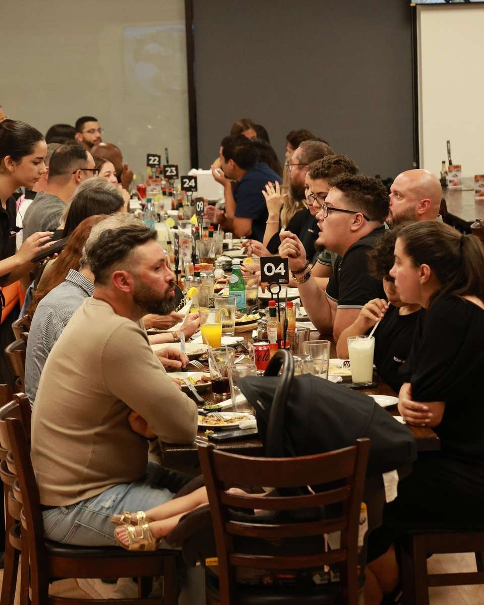 Bustling restaurant scene with a long communal table filled with diners enjoying grilled meats, cocktails, and fresh juices. The lively atmosphere features friendly conversations, attentive service, and a casual, modern dining vibe ideal for group gatherings or celebrations.