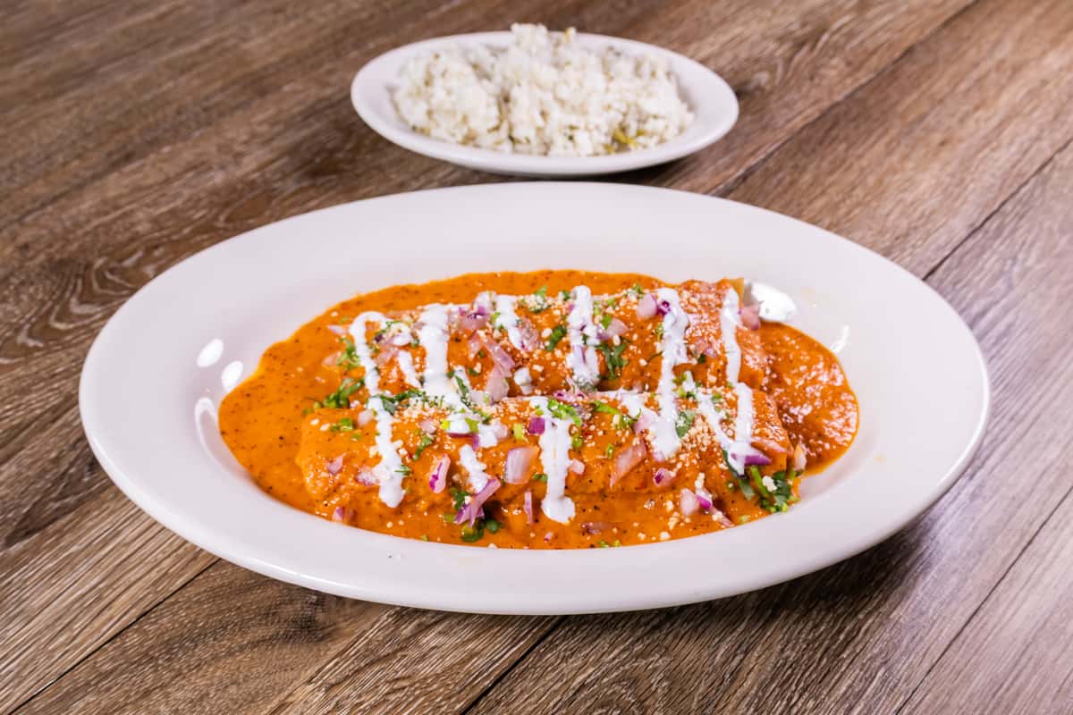 Creamy shrimp enchiladas topped with rich chipotle sauce, sour cream, diced red onions, cilantro, and crumbled queso fresco, served with a side of Mexican rice.
