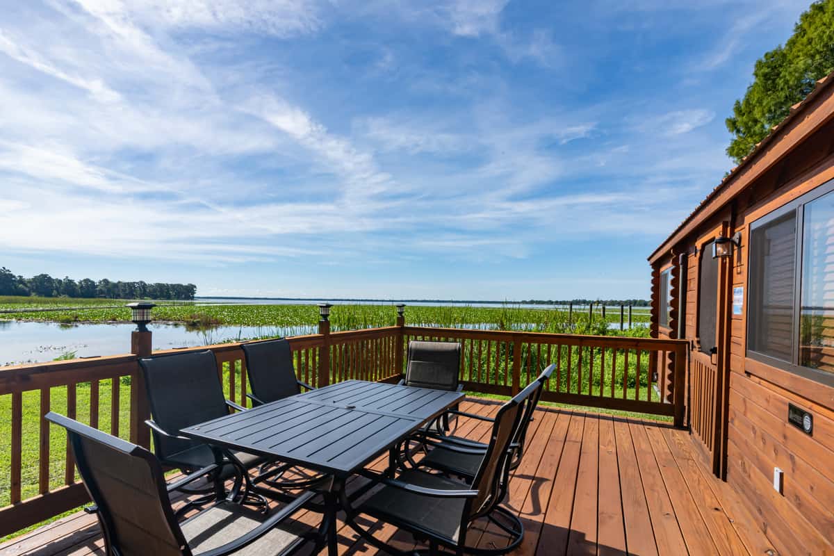 Scenic lakefront cabin deck with a black patio dining set overlooking tranquil waters and marsh grasses, offering peaceful outdoor seating at a Florida lakeside retreat.