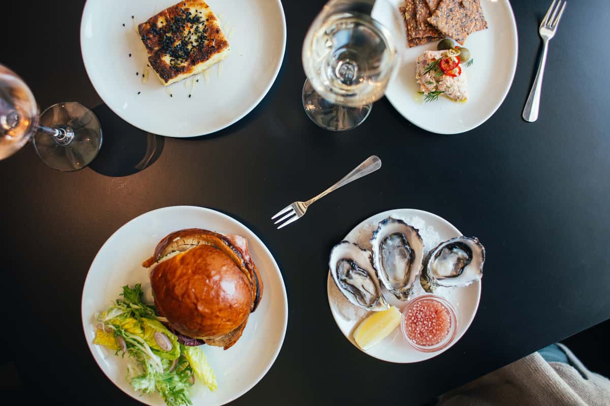 Plated appetizers, oysters on the half shell, and a gourmet sandwich served with wine