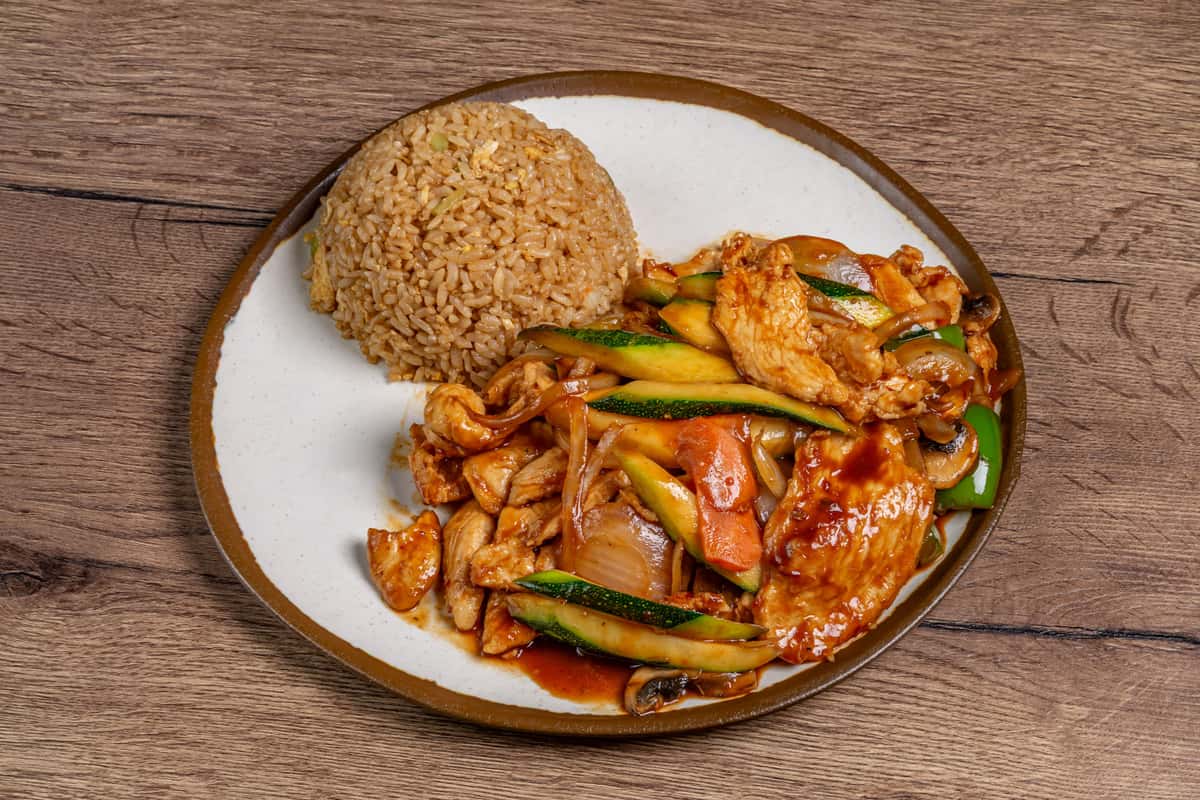 Stir-fried chicken with zucchini, onions, bell peppers, carrots, and mushrooms in a savory sauce, served alongside a portion of fried rice.