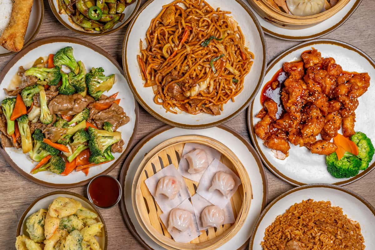 Assorted Chinese dishes including dumplings, noodles, fried rice, and stir-fried vegetables served on a wooden table.