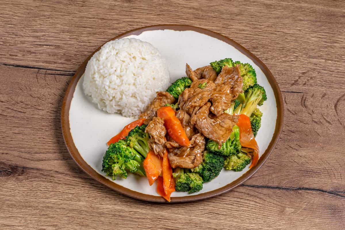 Beef and broccoli stir-fry served with sliced carrots in a savory sauce, accompanied by a mound of steamed white rice.