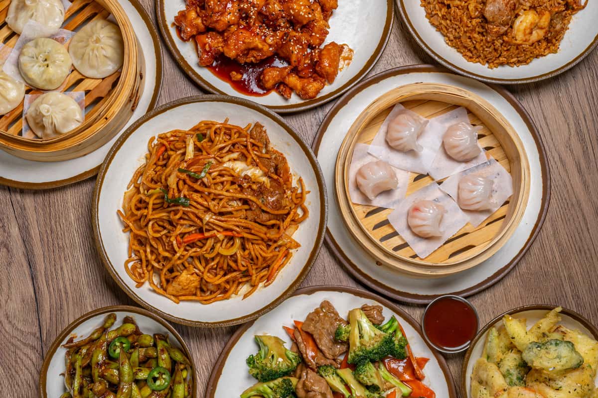 Assorted Chinese dishes including dumplings, noodles, fried rice, and stir-fried vegetables served on a wooden table.