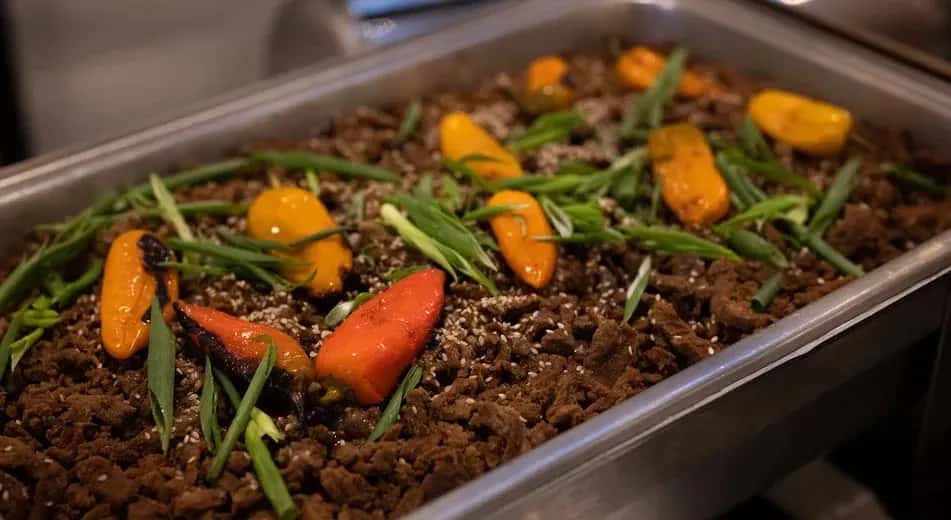 A chafing dish filled with a beef dish garnished with peppers and scallions